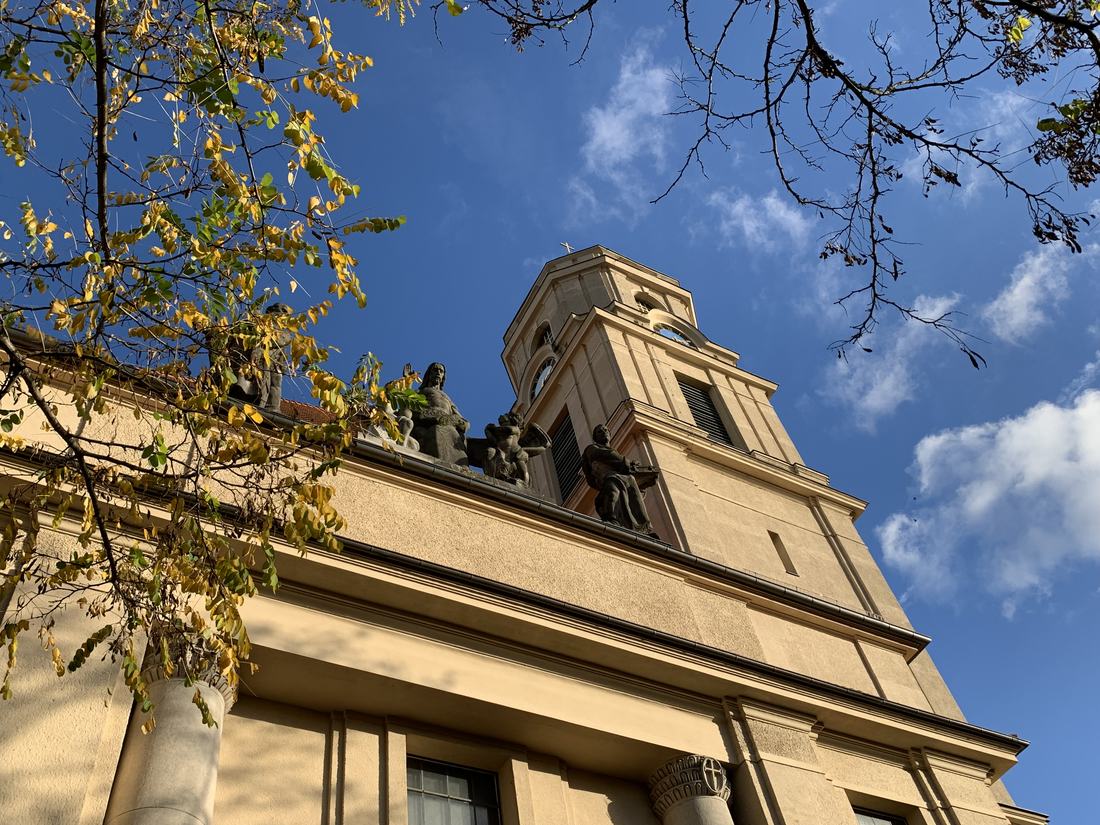 Turm und Fassade der Hoffnungskirche vor blauem Himmel, umrahmt von herbstlich gelbem Laub